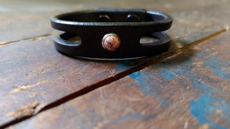 Puede incluir: Un brazalete de cuero negro con un dise&ntilde;o de doble capa y un acento de piedra rosa.