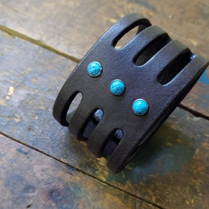 May include: A black leather bracelet with turquoise stones. The bracelet has a woven design and is adjustable.