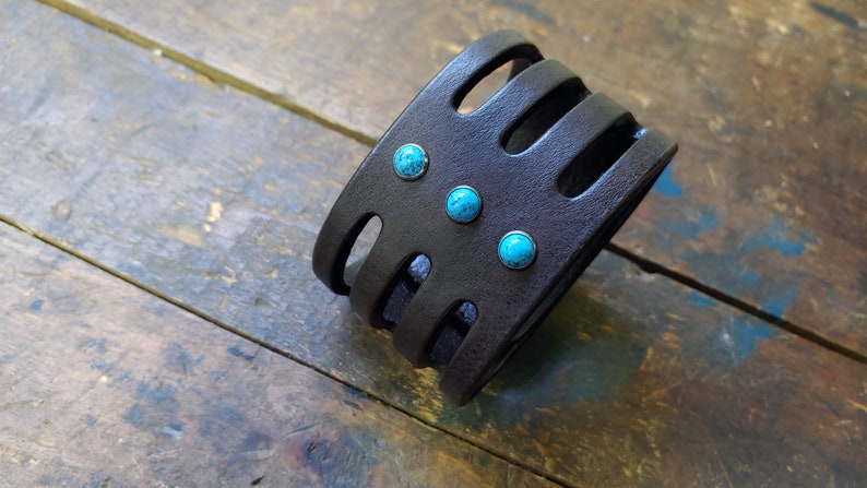 May include: A black leather bracelet with turquoise stones. The bracelet has a woven design and is adjustable.