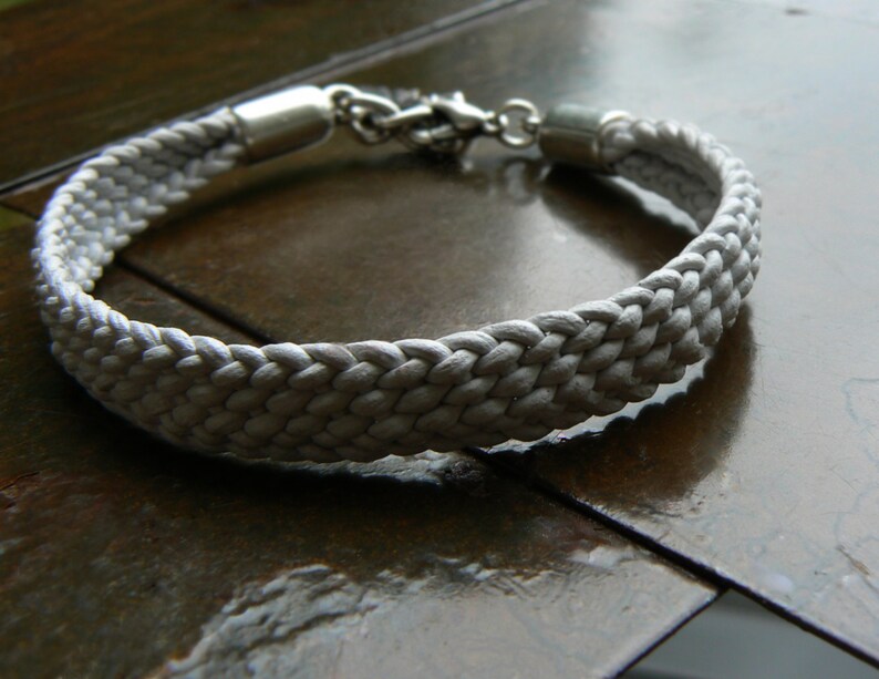 Puede incluir: Un brazalete de cuerda trenzada blanca con cierres de metal plateado.