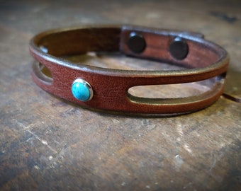 Op de afbeelding: Een bruin leren armband met een turquoise steen en een magneetsluiting.