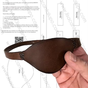 Puede incluir: Un parche de cuero marrón con una correa, sostenido por una mano. El parche está diseñado para cubrir el ojo izquierdo. El texto en el papel dice "Custom Leather for Patch Left Eye" y "www.lisacantalupo.com".
