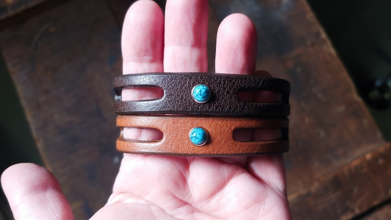 Puede incluir: Dos pulseras de cuero con piedras turquesa. La pulsera superior es de cuero marr&oacute;n y la pulsera inferior es de cuero marr&oacute;n.