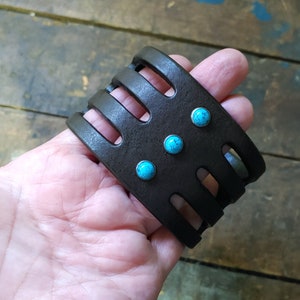 May include: A brown leather bracelet with a cut-out design and turquoise stones.