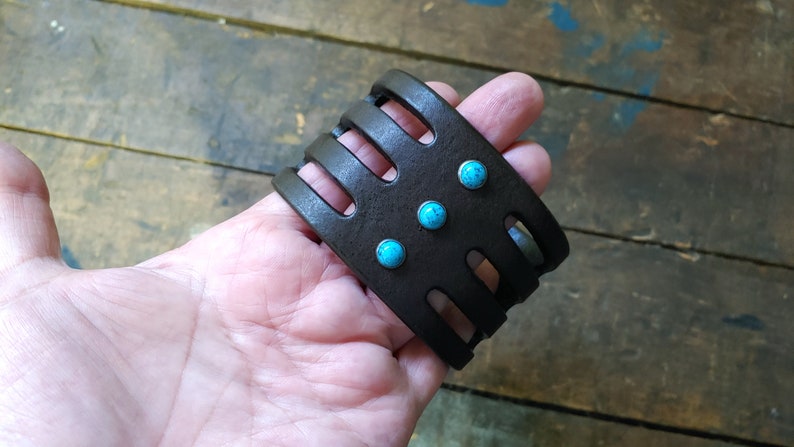 May include: A brown leather bracelet with a cut-out design and turquoise stones.