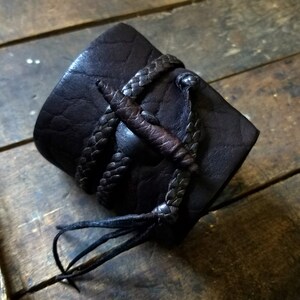 May include: Dark brown leather cuff bracelet with braided leather accents and a central decorative element. The cuff is approximately 2 inches wide and features a textured surface, with a braided leather strap.