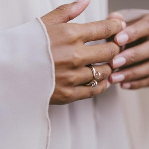 May include: A gold-colored ring with a spiral design. The ring is worn on a finger, with the spiral detail wrapping around the finger. The image is a close-up, highlighting the ring's design and the person's hand.
