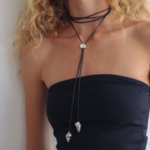 Op de afbeelding: Een zwarte leren choker met een zilveren hanger en twee zilveren schelpbedels.