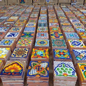 May include: A large collection of colorful, hand-painted ceramic tiles with intricate designs. The tiles are stacked in rows and feature a variety of floral, geometric, and abstract patterns.