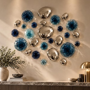 Puede incluir: Una instalación de arte mural compuesta por múltiples elementos circulares y de formas orgánicas en varios tamaños. La colección presenta una mezcla de esferas de vidrio translúcido azul profundo y discos de plata metálica pulida.