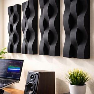 Puede incluir: Cuatro paneles acústicos negros con forma de onda montados en una pared. Un portátil, un altavoz y unos auriculares están sobre un escritorio de madera. También hay una pequeña planta en maceta sobre el escritorio.