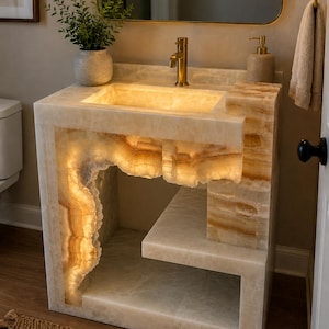 May include: A bathroom vanity crafted from translucent, cream-colored onyx stone with natural veining. The structure features an integrated sink, a lower shelf, and internal lighting that illuminates the stone's edges and textures from within.
