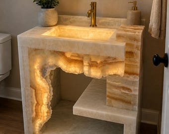 May include: A bathroom vanity crafted from translucent, cream-colored onyx stone with natural veining. The structure features an integrated sink, a lower shelf, and internal lighting that illuminates the stone's edges and textures from within.