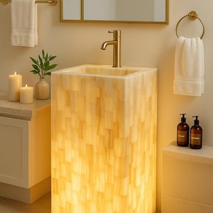 Può includere: Un moderno lavabo da bagno di forma rettangolare con una calda luce brillante. Il lavabo è realizzato in un materiale chiaro e strutturato. Un rubinetto dorato e un portasciugamani abbinato aggiungono un tocco di eleganza. Due flaconi di sapone e lozione sono su una mensola.