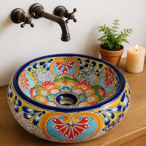 May include: A vibrant, hand-painted ceramic vessel sink with a colorful floral design. The sink features a blue rim and a detailed pattern in red, yellow, and orange. A bronze faucet is mounted on the wall above the sink.