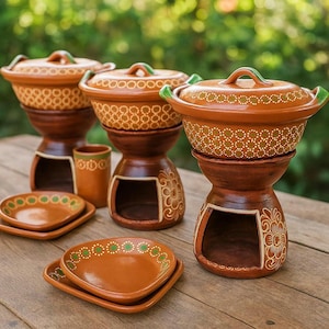 Può includere: Set di piatti da portata e scaldavivande in terracotta fatti a mano. Il set comprende ciotole con coperchio, piattini e una tazza, il tutto in tonalità marroni con accenti bianchi e verdi. I supporti hanno intagli decorativi.