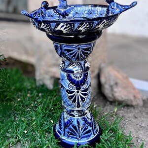Pode incluir: Banho de p&aacute;ssaros de cer&acirc;mica azul e branco com tr&ecirc;s p&aacute;ssaros empoleirados na borda. O banho de p&aacute;ssaros est&aacute; em um suporte alto e decorativo com um padr&atilde;o floral azul e branco.