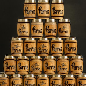 May include: A stack of wooden barrel-shaped tumblers with stainless steel rims. Each tumbler has the word "Parras" printed on it in a bold, black font. Some tumblers also feature a small graphic and additional text.