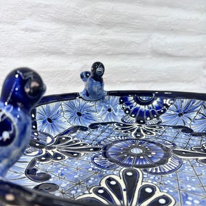 Pode incluir: Um prato de servir de cer&acirc;mica azul e branco com um design floral e tr&ecirc;s al&ccedil;as de p&aacute;ssaro. O prato &eacute; pintado &agrave; m&atilde;o com detalhes intrincados e tem uma borda festoneada.