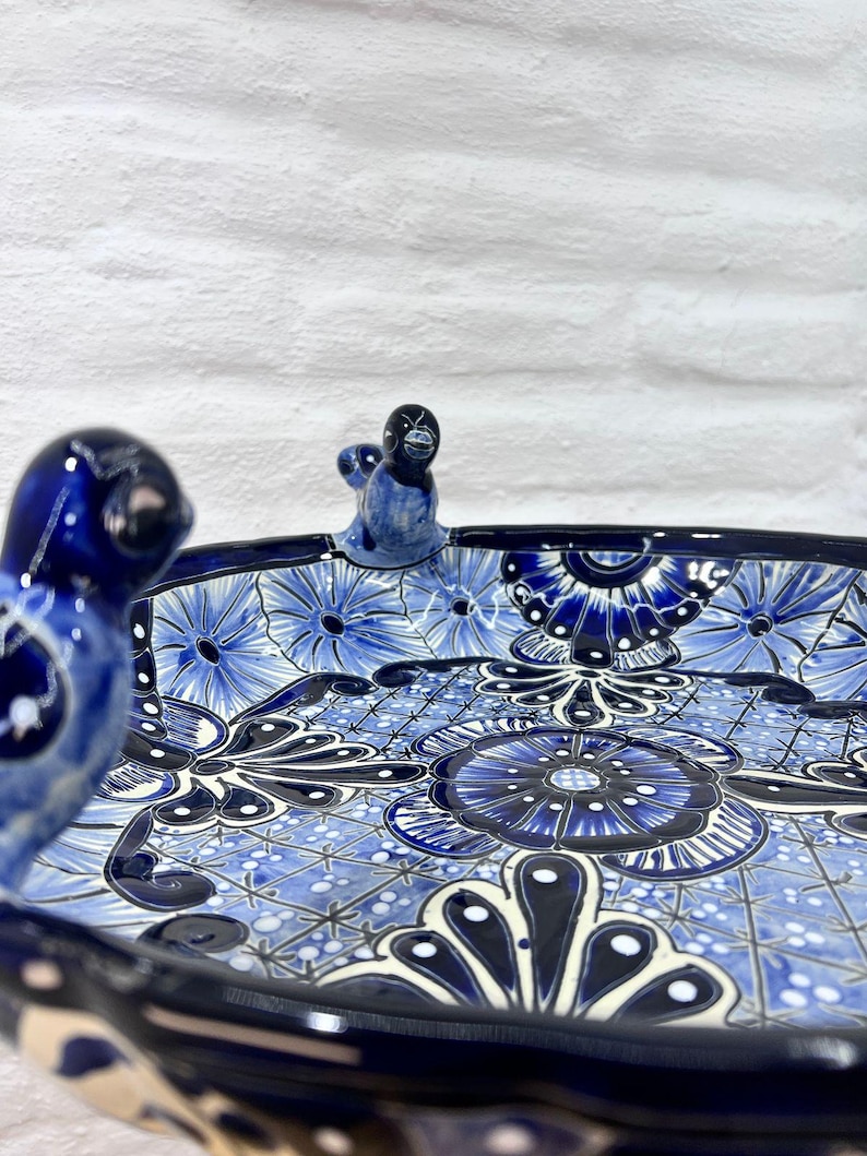 Pode incluir: Um prato de servir de cer&acirc;mica azul e branco com um design floral e tr&ecirc;s al&ccedil;as de p&aacute;ssaro. O prato &eacute; pintado &agrave; m&atilde;o com detalhes intrincados e tem uma borda festoneada.