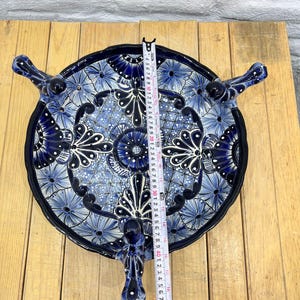 Pode incluir: Um prato de servir de cer&acirc;mica azul e branco com tr&ecirc;s pernas em forma de p&aacute;ssaros. O prato &eacute; decorado com um padr&atilde;o floral e tem um di&acirc;metro de aproximadamente 30 cm.