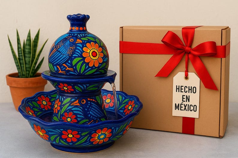 K&ouml;nnte beinhalten: Blaue Keramik-Brunnen mit Vogel- und Blumenmuster. Der Brunnen hat mehrere Ebenen und einen Wasserauslauf. Eine Geschenkbox mit rotem Band und einem Etikett mit der Aufschrift "HECHO EN M&Eacute;XICO" befindet sich daneben.