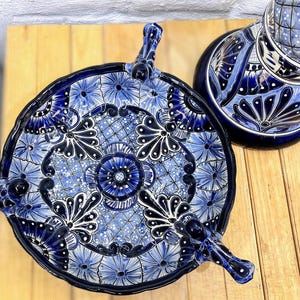 Pode incluir: Um prato de servir de cer&acirc;mica azul e branco com quatro pernas e um design floral. O prato &eacute; decorado com padr&otilde;es intrincados e redemoinhos.