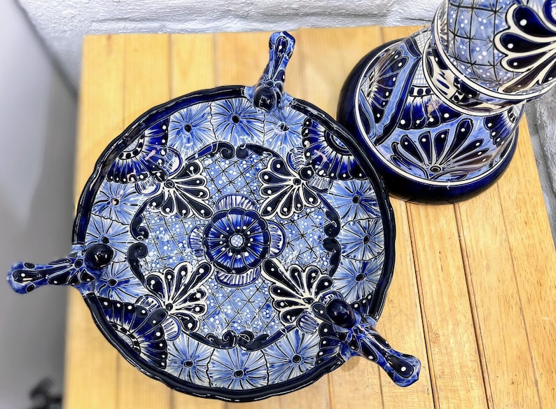 Pode incluir: Um prato de servir de cer&acirc;mica azul e branco com quatro pernas e um design floral. O prato &eacute; decorado com padr&otilde;es intrincados e redemoinhos.