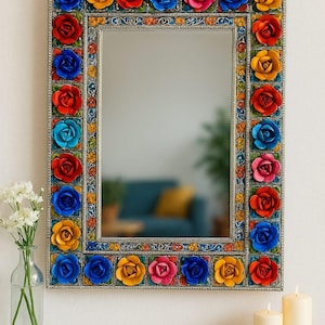 Puede incluir: Un espejo con marco plateado y un diseño floral colorido. El marco está decorado con flores 3D en tonos de rojo, azul, amarillo y rosa.