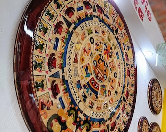 May include: A large, round, wooden wall hanging with a colorful, intricate design depicting the Aztec calendar. The calendar is surrounded by a dark brown wooden frame.