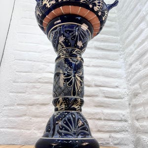 Pode incluir: Um bebedouro para p&aacute;ssaros de cer&acirc;mica azul e branco com um design floral decorativo. O bebedouro est&aacute; sobre um pedestal alto com uma base larga.