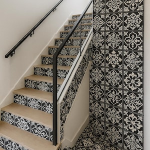 Puede incluir: Una escalera con escalones de madera clara y barandillas de metal negro. Las contrahuellas y la pared adyacente presentan un patrón de baldosas florales en blanco y negro que se repite. El suelo en la base de la escalera también tiene el mismo diseño de baldosas.