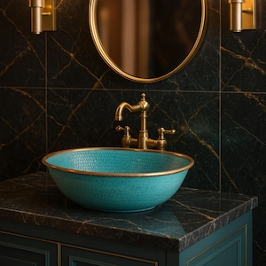 Puede incluir: Un lavabo turquesa texturizado con borde dorado se asienta sobre un mueble verde oscuro con ribetes dorados. Un grifo dorado y un espejo redondo están montados en una pared verde oscuro con aspecto de mármol. Dos apliques dorados flanquean el espejo.