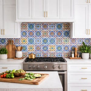 Puede incluir: Una cocina moderna con gabinetes blancos, herrajes dorados y un salpicadero estampado colorido. Una estufa de gas de acero inoxidable está centrada debajo del salpicadero. Una tabla de cortar de madera con comida está en la encimera.