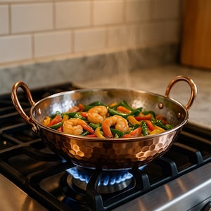 May include: A copper wok with a hammered texture, filled with cooked shrimp, green beans, and colorful bell peppers. The wok has two copper handles and is sitting on a gas stove with a blue flame.