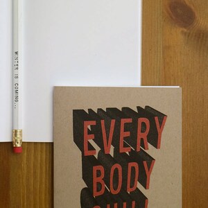 May include: A brown notebook with the text "EVERYBODY CHILL" in black and red letters. The text is in a 3D style with a shadow effect.