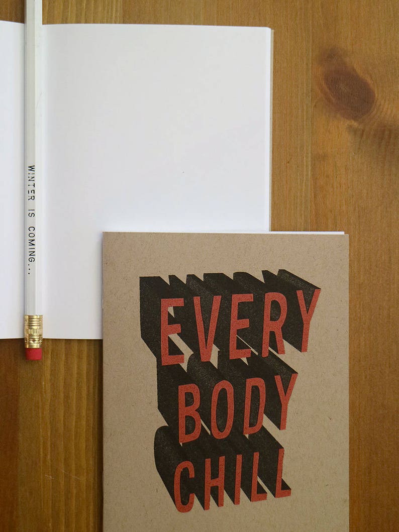 May include: A brown notebook with the text "EVERYBODY CHILL" in black and red letters. The text is in a 3D style with a shadow effect.
