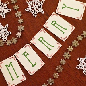 May include: A festive banner with the word "Merry" spelled out in green letters on white cards with red and green trim. The banner is decorated with a gold snowflake garland.