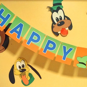 May include: A green, orange, and blue banner with the word "HAPPY" on it. There are two cartoon dog heads on either side of the banner. One dog is brown and the other is yellow.