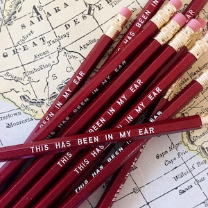 May include: A close-up of a stack of red pencils with white lettering that reads "This has been in my ear". The pencils are on top of a vintage map.
