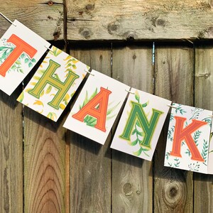 May include: A green and orange banner with the word "THANK" spelled out in large letters. The letters are surrounded by a leafy pattern.