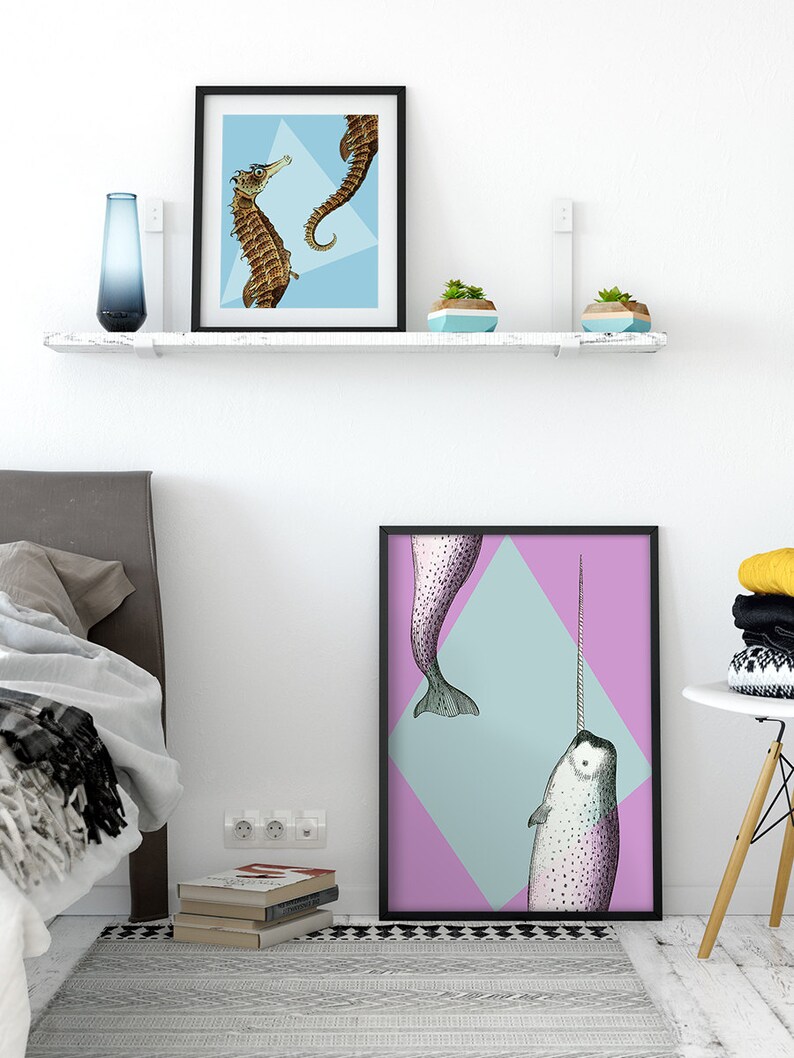 May include: Two framed art prints featuring sea creatures. One print shows two seahorses on a light blue background. The other print displays a narwhal with a long tusk against a pink and blue diamond.