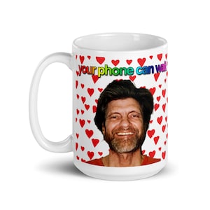 May include: White ceramic mug with a red heart pattern and the text "your phone can walk" in rainbow colors. A man with a beard and brown hair is pictured on the mug.