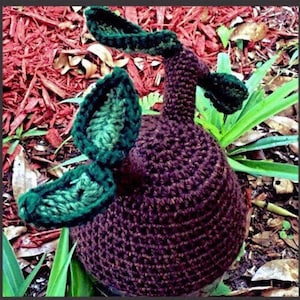May include: A crocheted brown and green plant hat with a textured surface. The hat has three green leaves on top.