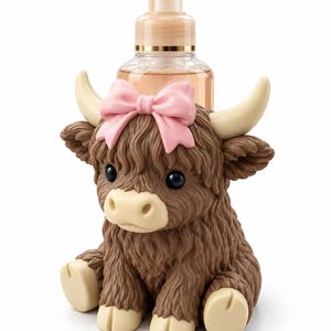 Può includere: Un dispenser di sapone in plastica trasparente con erogatore a pompa, inserito in una statuetta di mucca highland marrone e testurizzata. La mucca ha corna e zoccoli color crema, occhi neri e un fiocco rosa chiaro tra le orecchie.