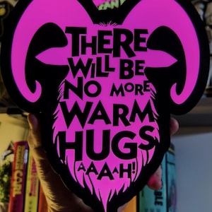 May include: A die-cut sticker featuring a bright pink ram head silhouette with black outlines. The text in black reads: THERE WILL BE NO MORE WARM HUGS AAAAH! The design has a bold, graphic style with sharp, stylised horns and a pointed chin area.