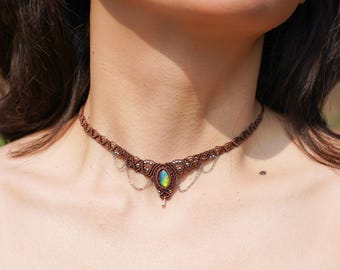 Op de afbeelding: Een bruine macramé choker ketting met een groen en blauwe iriserende edelsteen hanger en zilveren ketting accenten.