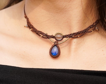 May include: A brown macrame choker necklace with a teardrop-shaped blue gemstone pendant and a round clear gemstone accent.