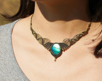 May include: A green and blue iridescent gemstone pendant necklace with a gold-colored cord and beads. The necklace is made with a macrame knotting technique.