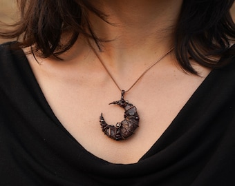 May include: A copper wire wrapped pendant necklace featuring a crescent moon shape with a dark brown gemstone.